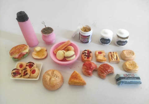 Conjunto de merienda que incluye mate, facturas y dulces en miniatura sobre una mesa.
