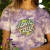 Blusa cropped feminina da marca Santa Cruz, com estampa colorida em fundo roxo.