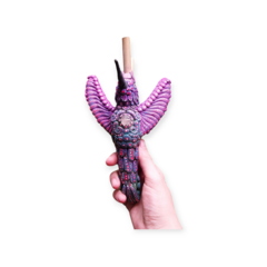 Kuripe Totem beija-flor colorido, com detalhes em pérolas e um bico longo, segurado por uma mão.