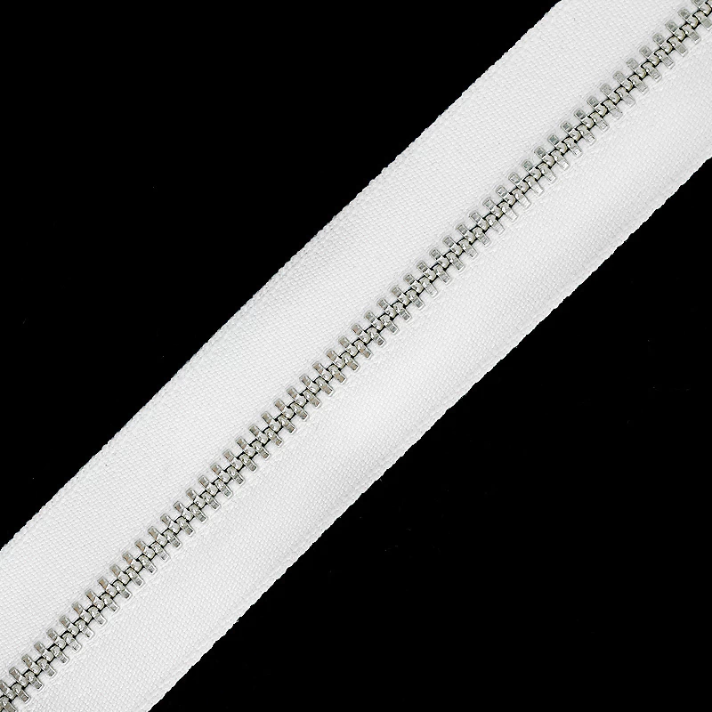 Zíper de metal niquelado YKK 045 para tingimento, vendido por metro, com fita branca e dentes metálicos.