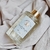 Frasco de spray aromático com fragrância de pera e frésia sobre um pano claro.
