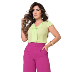 Mulher posando em uma blusa verde claro com laço e calça rosa, destacando um look elegante e vibrante.