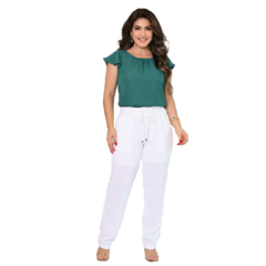 Mulher sorrindo, vestindo uma blusa verde e calças brancas, em um fundo branco.