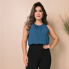 Mulher com blusa azul e calça preta, posando com um sorriso em um fundo neutro.