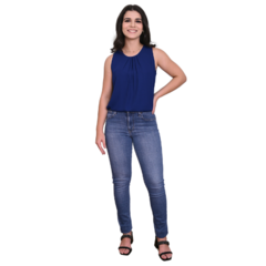 Mulher sorridente usando uma blusa azul e jeans, em pé com uma mão na cintura.