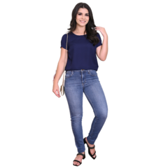 Mulher sorridente usando uma blusa azul escura e jeans, posando de forma casual.