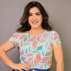 Mulher sorridente usando uma blusa colorida com estampa de folhas, posando com as mãos na cintura.