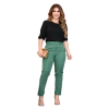Mulher posando com blusa preta e calça verde, segurando uma bolsa dourada.