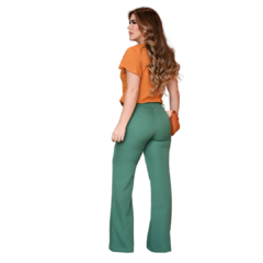 Mulher de costas usando blusa laranja e calça verde, com cabelo longo e ondulado.