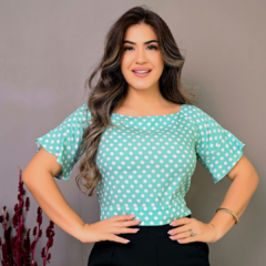 Mulher sorrindo com blusa verde água de bolinhas brancas, em fundo neutro.