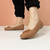 Mocassim feminino Modare na cor caramelo, com detalhe de laço, usado em um fundo rosa.