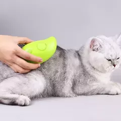 Um gato cinza sendo escovado com uma escova vapor elétrica verde, enquanto uma mão segura o dispositivo.
