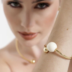 Bracelete dourado com aro liso e esfera resinada em cor clara.