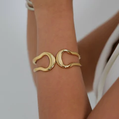 Bracelete liso em formato orgânico torcido, com dois lados se encontrado ao centro, banhado a Ouro 18k ou Ródio Branco.