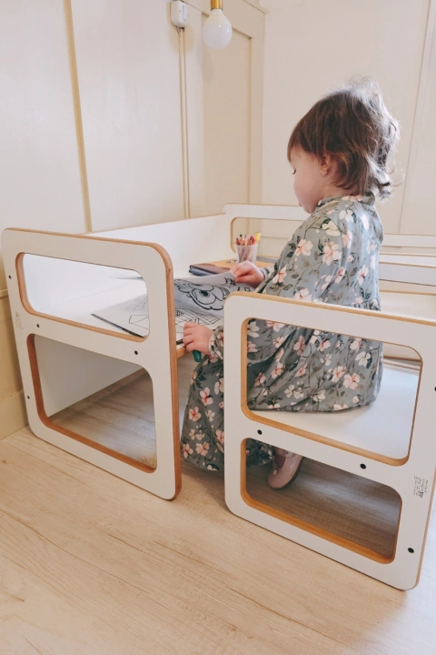 Niña dibujando en la Mesa Multifuncional 3 en 1 de madera blanca, acompañada de sillas convertibles.