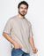 Camiseta oversized de algodão em tom areia, modelagem solta, usada por um homem sorridente.