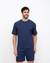 Homem sorridente usando camiseta e shorts na cor azul marinho, posando contra um fundo branco.