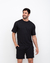 Homem sorridente vestindo uma camiseta oversized preta de modal, combinada com shorts pretos, posando em fundo branco.