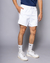 Homem usando shorts fitness brancos, com camiseta azul e tênis brancos, posando em fundo cinza.