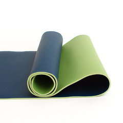 Mat de yoga Adho Mukha Everyday de 4 mm de espesor en colores verde y azul, enrollado sobre una superficie blanca.