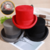 Conjunto de chapéus cartola em diferentes cores: vermelho, cinza e preto, sobre uma superfície neutra.