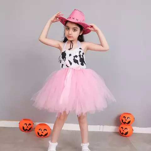 Menina vestindo fantasia de vaqueira infantil com saia de tule rosa e chapéu rosa, em frente a abóboras decorativas.