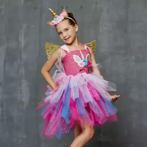 Menina vestindo uma fantasia de unicórnio rosa com asas douradas e tiara, posando sorridente.