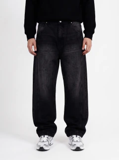 Pantalones vaqueros negros holgados modelo 'TID IND' con efecto desgastado y bolsillos delanteros, combinados con zapatillas deportivas blancas.