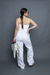 Modelo feminina usando macacão off white com botões, vista de costas, segurando uma bolsa com lenço.