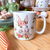 Caneca branca com estampa de coelhinha floral, decorada com flores e borboletas, ideal para a Páscoa.