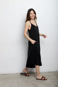 Mujer usando un Mono Over Basic de color negro, con tirantes finos y sandalias marrones, caminando y sonriendo