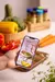 Imagem de uma mão segurando um smartphone exibindo a capa do eBook "Jantares Completos", com legumes frescos ao fundo.