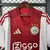 Camisa titular do Ajax 2025/26 com listras vermelha e branca, patrocinador Ziggo, escudo com três estrelas e detalhes da Adidas
