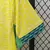 Camisa titular feminina da Seleção Brasileira 2024 na cor amarela com grafismos em tom claro, escudo azul da CBF com cinco estrelas, gola verde e detalhes nos punhos em azul e verde