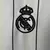 Camisa branca do Real Madrid US Pack 2025/26 da Adidas, modelo edição especial estilo beisebol, com listras verticais finas, gola em V com botões e escudo bordado no peito preta e branca e detalhes verde fluorescente