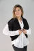 Modelo con chaleco corto tejido negro sobre una blusa blanca, sonriendo y posando.