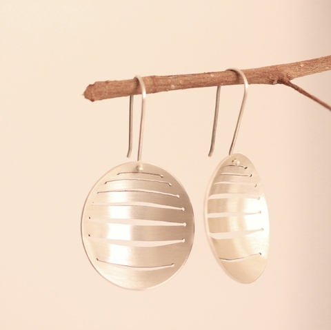 Brinco Vasarely pendurado em um galho, com design circular e linhas horizontais.