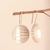 Brinco Vasarely pendurado em um galho, com design circular e linhas horizontais.