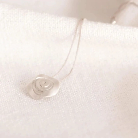 Colar prateado com um pingente com design delicado e moderno sobre um fundo claro.