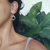 Modelo usando brinco de prata em formato de gota, com planta ao fundo.