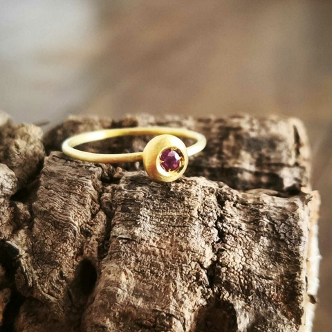 Anel dourado com uma pedra de rubi, sobre uma superfície de madeira.
