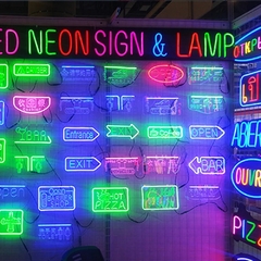 Várias placas de neon iluminadas em diferentes cores, exibindo sinais como "Open", "Exit", "Bar", e "Hot Pizza".