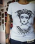 Blusinha branca com ilustração estilo old school de Frida Kahlo com olhos brancos, coroa de folhas com caveira e colar de teia de aranha.