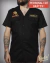 Black short-sleeve work shirt with skull and wrench design on left chest and customizable name patch on right chest, worn by tattooed man