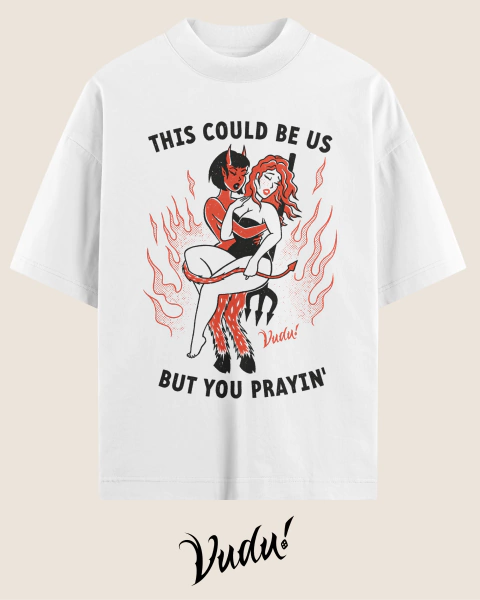 Camisa oversized branca com estampa que apresenta duas figuras estilizadas, uma mulher demoníaca e outra com cabelo ruivo, acompanhadas pela frase "THIS COULD BE US BUT YOU PRAYIN'".
