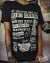 Camiseta preta estilo cartaz de show com “Riot Grrrl Punk Fest” e nomes de bandas punk feministas.