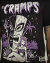 Camiseta preta com Poison Ivy, dos The Cramps, em estilo tiki, usando roupa de onça, cercada por caveiras e totem na selva.
