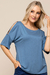 Modelo vestindo blusa visco crepe azul claro com detalhes de fenda no ombro com botão, e mangas curtas.