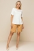 Modelo vestindo uma blusa crepe linho branca com mangas curtas e detalhes em botão, acompanhada de shorts bege.