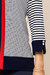Detalhe de um cardigan listrado em azul marinho e branco, com uma faixa vermelha e botões nos punhos.